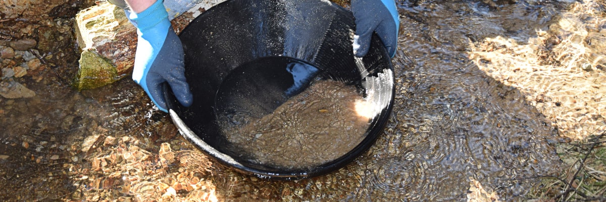 Ein Goldsucher sucht mit einer Waschpfanne nach Gold in einem Bach im Erzgebirge